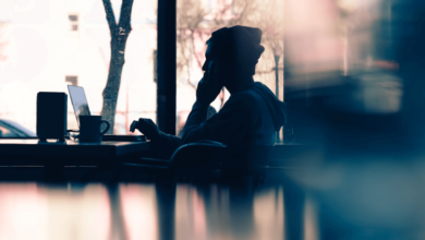 A person in a beanie working on their laptop with a mug of coffee in front of them.