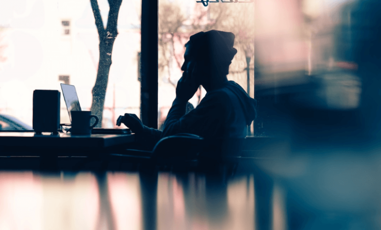 A person in a beanie working on their laptop with a mug of coffee in front of them.